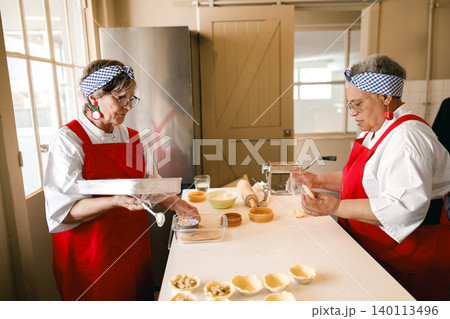 Senior Caucasian and Black women baking pastries in a professional kitchen setting Senior Caucasian and Black women baking pastries in a professional kitchen setting 140113496