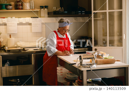 Senior Black woman pastry chef preparing dough in a professional commercial kitchen bakery workshop 140113509