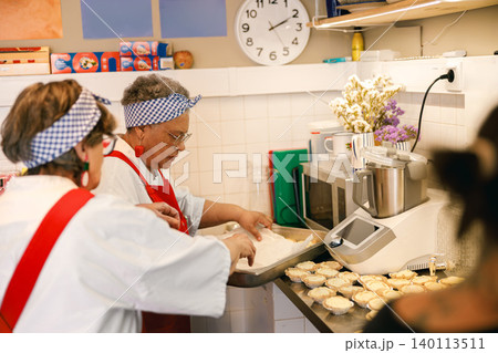 Two senior multiracial women baking sweet pastries in a commercial kitchen 140113511