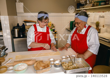 Happy senior Caucasian and Hispanic female chefs preparing dough in a professional kitchen bakery. 140113528