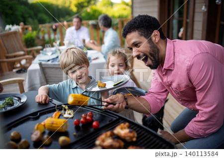 Man grilling meat and vegetable on grill during family summer garden party. Man grilling meat and vegetable on grill during family summer garden party. 140113584