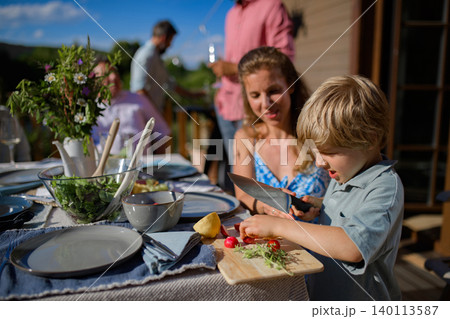 Young boy helping mom with cutting vegetables for bbq party. 140113587