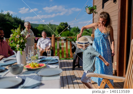 Family with kids having fun at barbecue party dinner on patio, people sitting at table on patio and talking 140113589