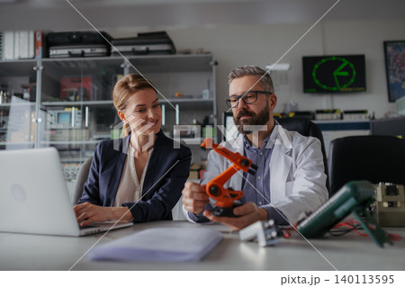 Robotics engineers working on laptop and desinging modern robotic arm in laboratory. Robotics engineers working on laptop and desinging modern robotic arm in laboratory. 140113595