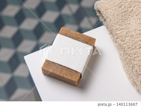 Brown soap with blank paper label mockup near beige towel in blue bathroom. Unbranded packaging Brown soap with blank paper label mockup near beige towel in blue bathroom. Unbranded packaging 140113687