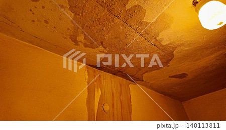 Water damage and stains on a textured ceiling and wall with a light fixture. Visible signs of water infiltration and damage are evident on the textured ceiling and adjacent wall, with staining and Water damage and stains on a textured ceiling and wall with a light fixture. Visible signs of water infiltration and damage are evident on the textured ceiling and adjacent wall, with staining and 140113811