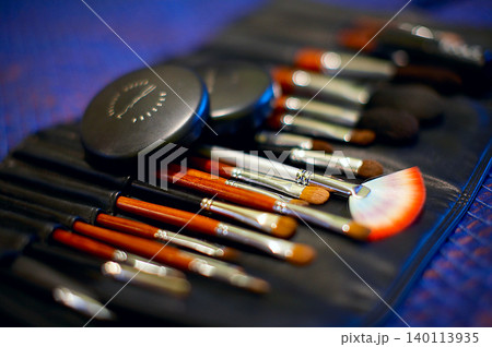 Professional makeup brush set in black leather roll case with compact powder on blue background 140113935