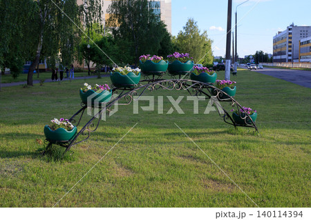 Wrought iron flower arch with green petunia pots on lawn grass, urban street landscape design element Wrought iron flower arch with green petunia pots on lawn grass, urban street landscape design element 140114394