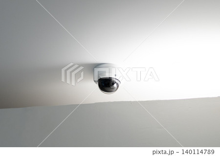 Dome security camera mounted on white ceiling with bright light reflection Dome security camera mounted on white ceiling with bright light reflection 140114789