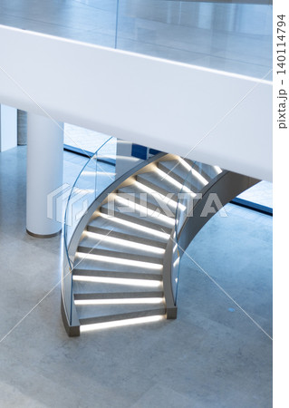 Curved staircase with illuminated steps and glass railing in modern interior 140114794