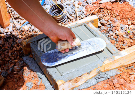 Worker levels fresh concrete with trowel on wooden frame at construction site Worker levels fresh concrete with trowel on wooden frame at construction site 140115124