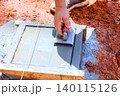 Worker uses trowel to spread edge concrete into wooden mold on construction site 140115126