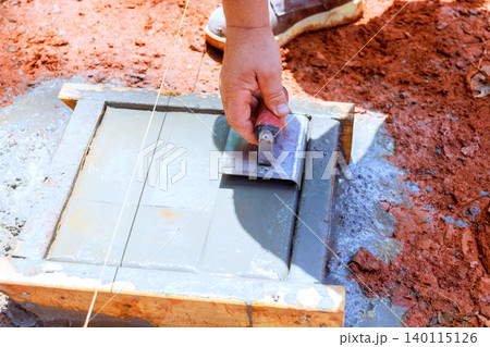 Worker uses trowel to spread edge concrete into wooden mold on construction site Worker uses trowel to spread edge concrete into wooden mold on construction site 140115126