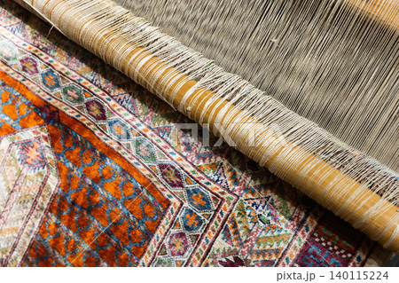 Close-up of a handwoven Persian rug on a loom, highlighting colorful geometric patterns 140115224