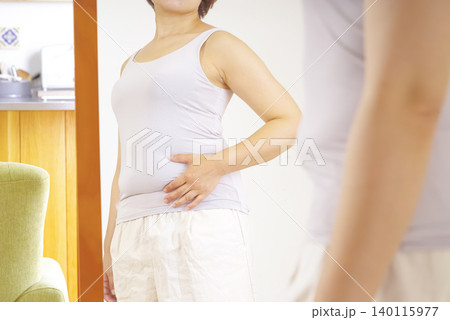 鏡の前でぽっこりお腹を気にする女性 鏡の前でぽっこりお腹を気にする女性 140115977