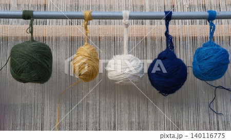 Balls of colored yarn on metal bar of rug-weaving loom. Ancient carpet weaving craft, workshops and regional and international festivals. Creating traditional oriental rugs. Textile texture Balls of colored yarn on metal bar of rug-weaving loom. Ancient carpet weaving craft, workshops and regional and international festivals. Creating traditional oriental rugs. Textile texture 140116775