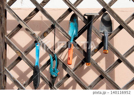 Garden hand tools hanging on a planter trellis. Garden hand tools hanging on a planter trellis. 140116952