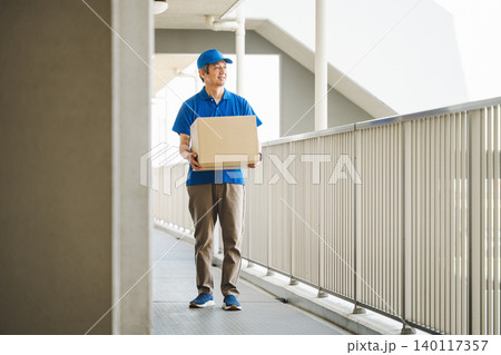 マンションへ荷物を運ぶ宅配業者の男性 マンションへ荷物を運ぶ宅配業者の男性 140117357