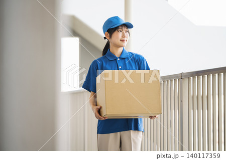 マンションに荷物を運ぶ宅配便業者の若い女性 マンションに荷物を運ぶ宅配便業者の若い女性 140117359