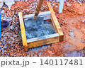 Workers set shovel in wet cement inside wooden frame at construction site 140117481