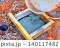 Worker pours concrete from container into wooden mold at construction site during work hours. 140117482
