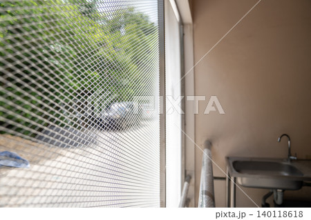 An old balcony service area has anti bird netting fixed along the open side, includes a small sink, narrow space, and metal lattice detail for building maintenance use. 140118618