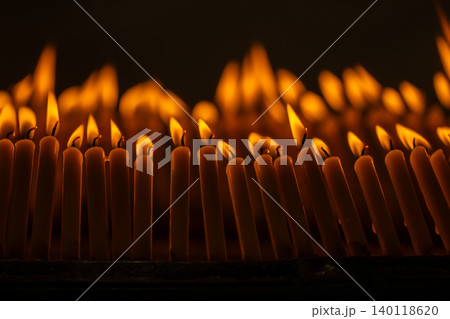 Close up rows of small burning candles capture soft smoke, flickering firelight, and an emotional low light moment of prayer and remembrance. Close up rows of small burning candles capture soft smoke, flickering firelight, and an emotional low light moment of prayer and remembrance. 140118620