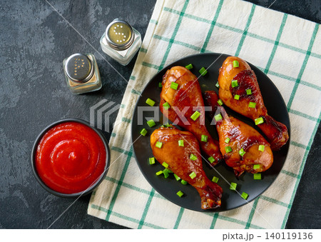Fried chicken legs with sauce on a black table, top view. Roast chicken drumsticks with ketchup. Fried chicken legs with sauce on a black table, top view. Roast chicken drumsticks with ketchup. 140119136