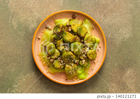 Brussels sprouts and zucchini slices are on a plate and topped with chopped walnuts. This dish can be served for breakfast or lunch. It is a healthy choice for any meal 140121271