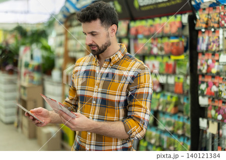 Adult man selects packets of seeds at gardening supermarket 140121384