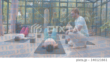 Guiding coach kneeling beside central student in teal leggings correcting posture on mats in studio Guiding coach kneeling beside central student in teal leggings correcting posture on mats in studio 140121661