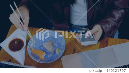 Picking sushi, Asian woman in leather jacket at wooden table, holding chopsticks and phone, laptop Picking sushi, Asian woman in leather jacket at wooden table, holding chopsticks and phone, laptop 140121797