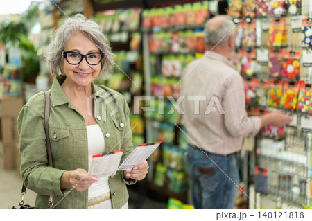 Mature woman selects packets of seeds at gardening supermarket Mature woman selects packets of seeds at gardening supermarket 140121818