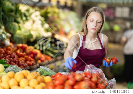 Girl shop seller add tomato goods on display case in vegetable store 140121893