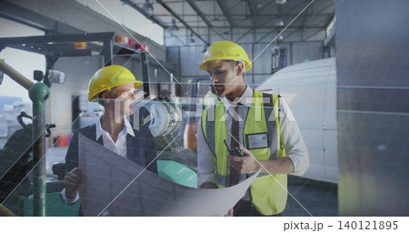 Examining two construction workers wearing yellow hardhats and vest in hangar, holding blueprint 140121895