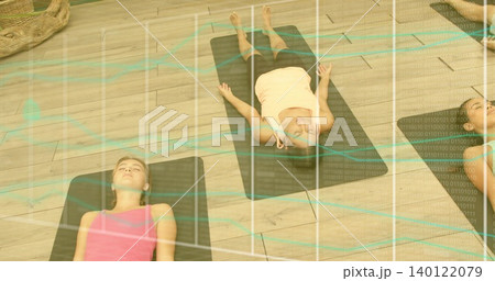 Lying yoga group supine in studio on black mats, wearing tanks, with woven basket and overlay Lying yoga group supine in studio on black mats, wearing tanks, with woven basket and overlay 140122079