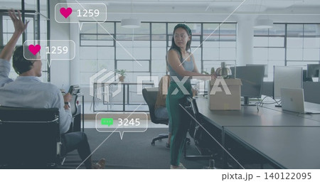 Holding cardboard box and metal kettle, woman wearing gray tank and green pants in open-plan office 140122095