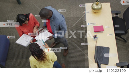 Leaning team in coral, denim, yellow reviewing clipboards and documents at office desk, with laptop 140122190