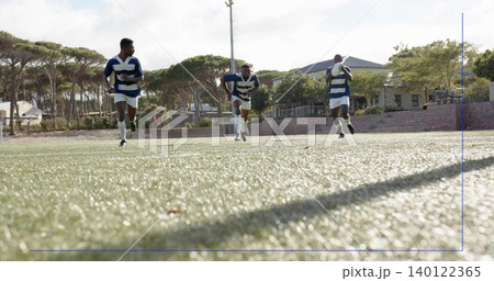 Sprinting three rugby players running on artificial turf at park, in striped jerseys and cleats Sprinting three rugby players running on artificial turf at park, in striped jerseys and cleats 140122365