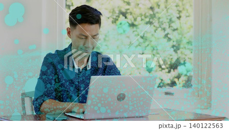Typing adult Asian man in blue shirt using laptop at desk by window, with turquoise overlay Typing adult Asian man in blue shirt using laptop at desk by window, with turquoise overlay 140122563