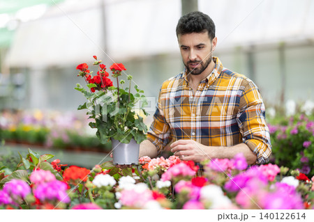 In flower shop, male customer with geranium in hands became interested in product In flower shop, male customer with geranium in hands became interested in product 140122614