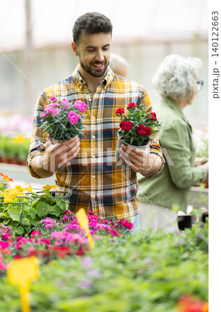 Adult man choosing garden carnation in pot at flower shop Adult man choosing garden carnation in pot at flower shop 140122663