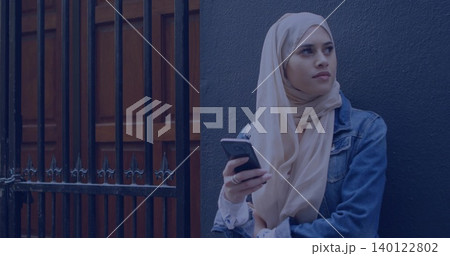 Holding woman in beige scarf, denim jacket checking smartphone by metal gate, copy space Holding woman in beige scarf, denim jacket checking smartphone by metal gate, copy space 140122802