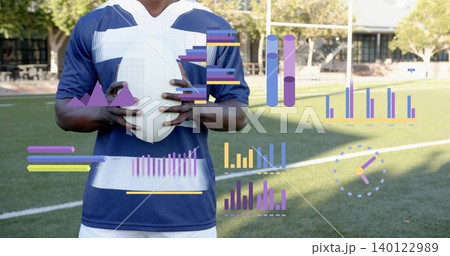 Holding white football, male athlete wearing navy blue and white jersey on turf with AR charts Holding white football, male athlete wearing navy blue and white jersey on turf with AR charts 140122989