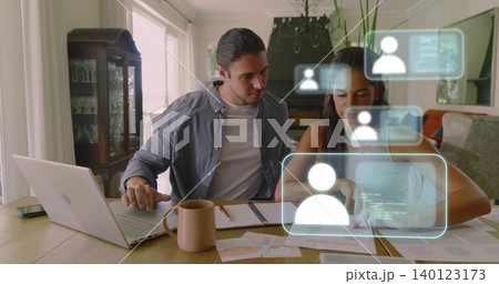Reviewing couple collaborating at home wood table, using laptop, documents and holographic UI Reviewing couple collaborating at home wood table, using laptop, documents and holographic UI 140123173