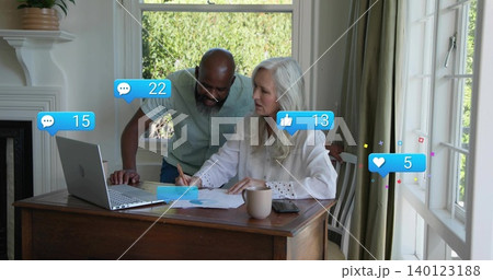 Working senior couple wearing light clothing, reviewing forms at home desk with laptop and likes Working senior couple wearing light clothing, reviewing forms at home desk with laptop and likes 140123188