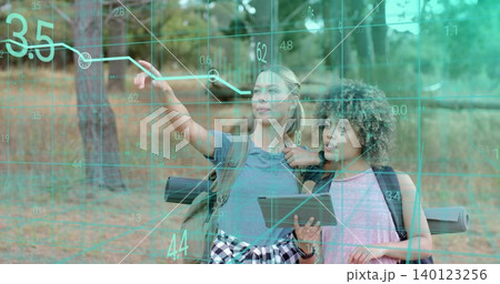 Pointing two hikers examining AR grid in wooded clearing, holding tablet and packs with mats 140123256