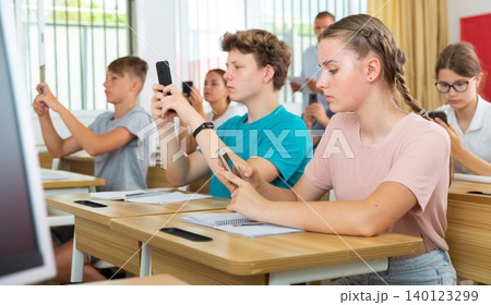 Teenager students sitting in class room with smartphones Teenager students sitting in class room with smartphones 140123299