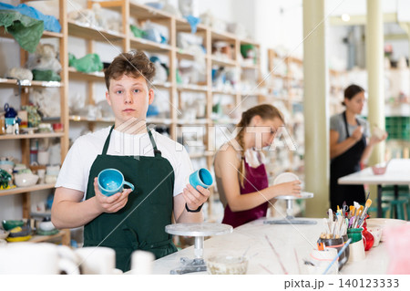 Teen boy posing with ceramic cup in ceramic workshop 140123333