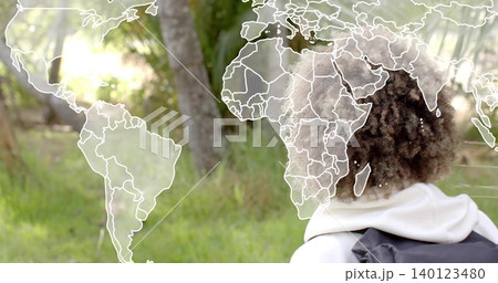 Standing woman facing grass, trees wearing white hoodie and dark backpack map overlay, copy space 140123480